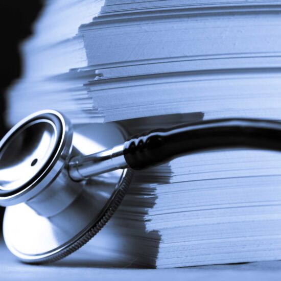 Photo of a stethoscope laying next to a large stack of papers