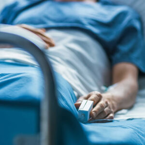 Patient in hospital bed with monitoring device on their index finger