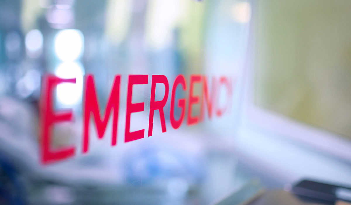 A glass window of an emergency department with the word "Emergency" stenciled on it.