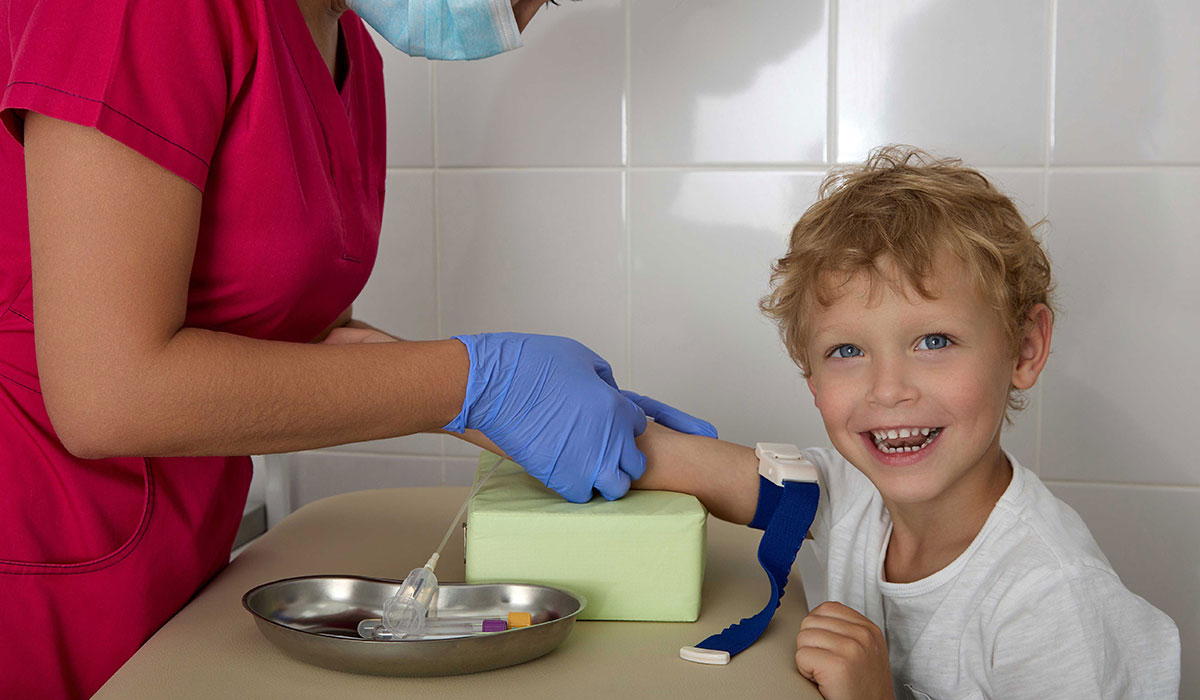 Child smiling at the camera while getting his blood drawn