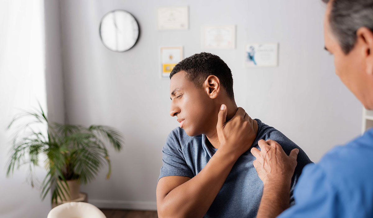 Patient clutching his neck in pain during an examination in the doctor's office