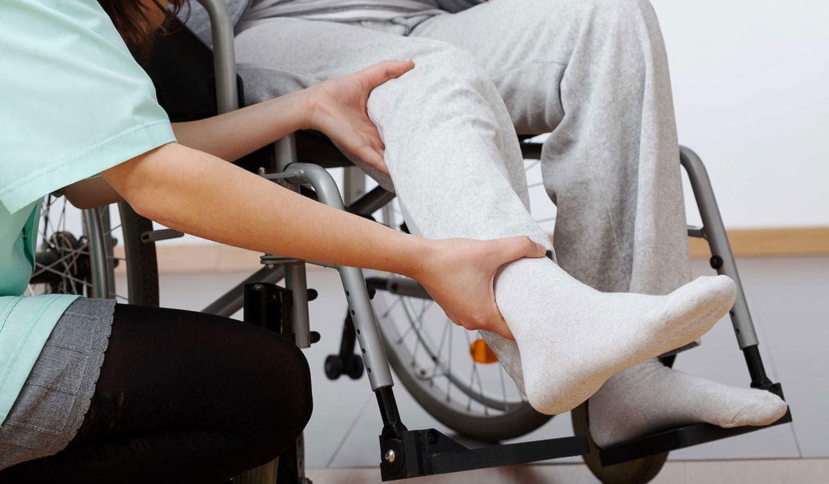 A medical professional examining the leg of a patient using a wheelchair.